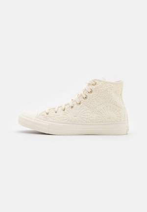 Højt sneakers i off-white med blonder blomster mønster, hvid gummisål og hvide snørebånd med gyldne huller, set fra siden.