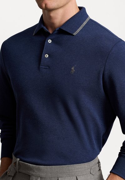 Tumši zilas krāsas garām piedurknēm polo krekls ar pelēku svītrotu apkakli, ar trim pogām un nelielu izšūtu logo kreisajā krūtī.