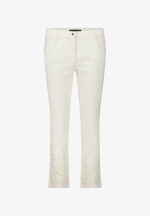 Białe dżinsowe spodnie z rozkloszowanymi nogawkami, ozdobione kwiatowymi wycięciami na dolnej krawędzi oraz subtelnymi metalicznymi zdobieniami wzdłuż brzegów.
