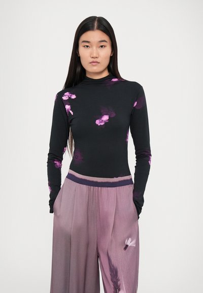 Long-sleeve black top with purple floral design. Paired with light purple, loose-fitting pants featuring a textured finish and elastic waistband.