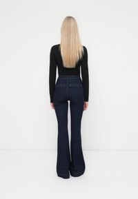 Pantalons en denim taille haute évasés en bleu foncé, dotés de deux poches arrière et de détails de couture subtils le long de l'ourlet.