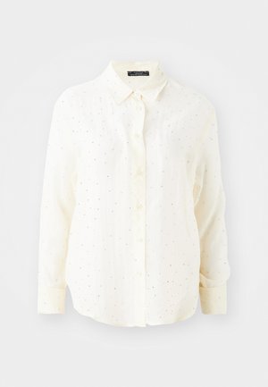 Chemise à manches longues en crème avec col boutonné, présentant une légère texture et des accents de points argentés dispersés.