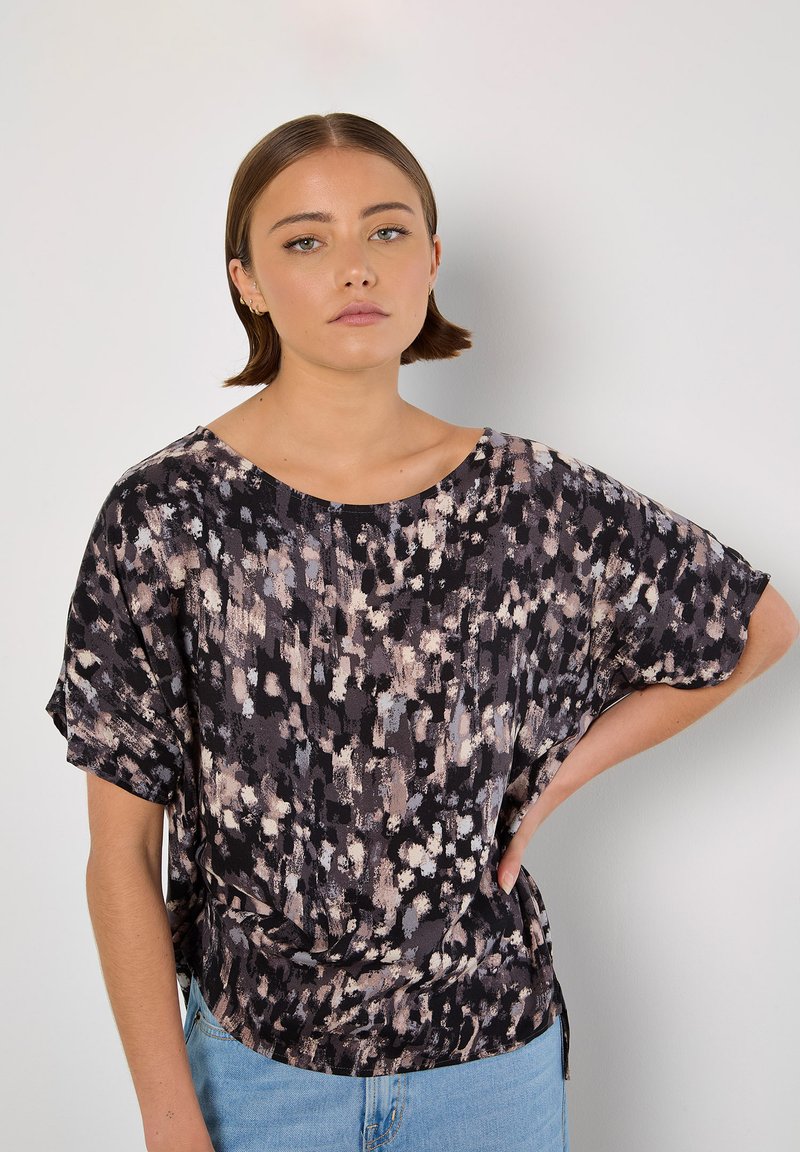 Schwarze Bluse mit lockerer Passform, die ein gesprenkeltes Muster in Creme- und Rosatönen aufweist. Kurze Ärmel mit einem kreativen Halsausschnitt und seitlichen Schlitzen.