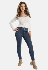 Jeans elasticizzati blu navy con design aderente, dotati di due tasche frontali e una texture liscia. Abbinati a un top bianco a maniche lunghe.