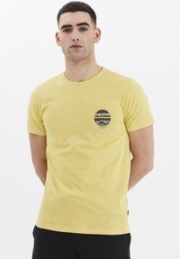 Gul bomulds t-shirt med korte ærmer og rund hals. Har et trykt rundt logo med "CALIFORNIA" og bjergdesign på brystet.