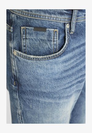 Traperice svijetloplave boje s istrošenom teksturom. Imaju džep za novčiće, kontrastne žute šavove i crnu oznaku na stražnjem džepu.