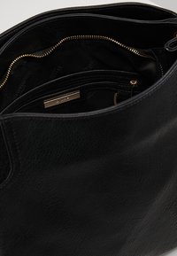 Černá kožená kabelka typu tote s hladkou texturou, uvnitř vybavená kapsou na zip a zlatavým kováním. Prostorný interiér s několika přihrádkami.