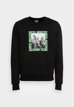 Czarna długorękawowa bluza z centralnym kwadratowym grafiką z rozmytymi postaciami, otoczona jasnooliwkowymi napisami "DIESEL INDUSTRY" z każdej strony.