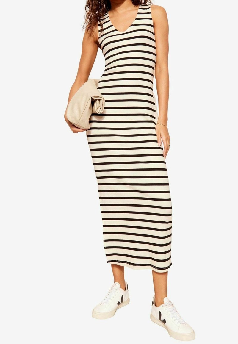 Robe midi rayée crème et noire, coupe ajustée avec décolleté en V sans manches. Associée à des baskets blanches et une pochette beige.