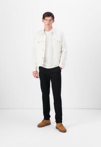 White denim jacket over a white t-shirt, paired with black trousers and brown lace-up shoes. Simple design with no visible patterns or accents.