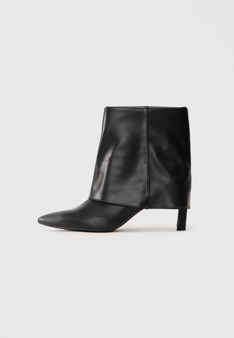 Black leather mid-calf boot with pointed toe, folded upper shaft, and slender low heel standing on white background.
