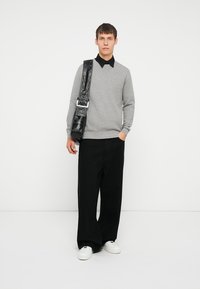 Grå stickad tröja med ett texturerat mönster, svart skjorta med krage, vida svarta byxor och vita sneakers. Svart väska med axelrem.