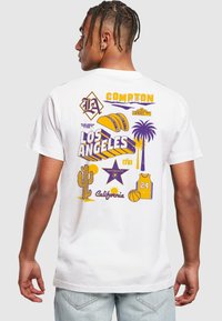 Biela bavlnená tričko s farebnou grafikou vrátane paliem, kaktusov a športových ikon, s textom "Compton" a "Los Angeles" v purpurovej a žltej farbe.