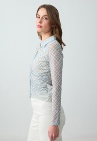 Camicia a quadri blu chiaro e gialla con colletto, maniche lunghe trasparenti e dettaglio arricciato sul davanti. Realizzata in tessuto leggero e dalla consistenza texture.