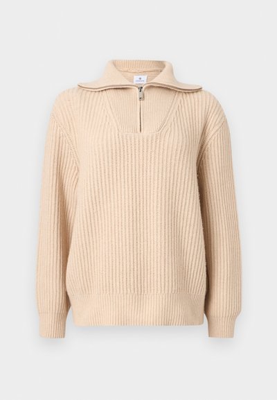 Pull en tricot côtelé beige avec manches longues, col à demi-fermeture éclair, et larges poignets et ourlet côtelés.