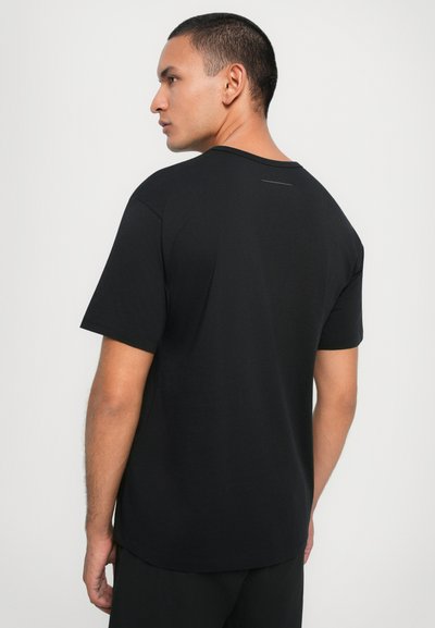 T-shirt en coton noir vu de dos, avec un col rond, des manches courtes et un subtil detail de couture verticale près de l'encolure.