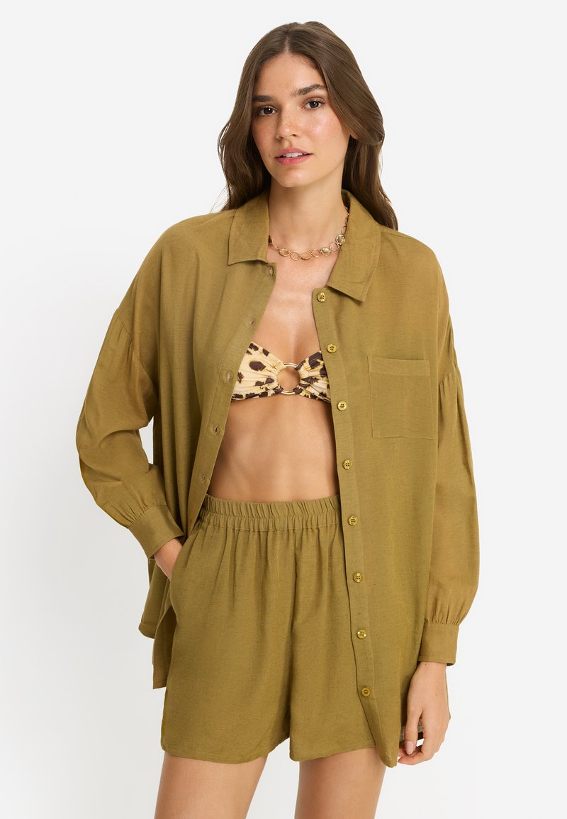 Πουκάμισο χρώματος ελιάς με κουμπιά, χαλαρή εφαρμογή και μακριά μανίκια, συνδυασμένο με σορτς στο ίδιο χρώμα· διαθέτει τσέπη και απαλή υφή.