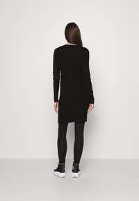 Černé pletené šaty s dlouhými rukávy, délka ke kolenům, nošené přes černé legíny, doplněné černými vysokými teniskami, minimalistický styl.