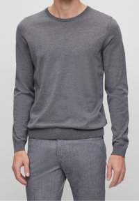 Szary sweter typu crew-neck wykonany z miękkiego materiału, z długimi rękawami i żebrowanymi mankietami. Lekko dopasowany krój o gładkiej fakturze.