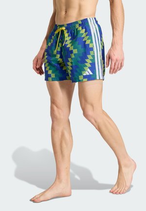 Modré plavky se zeleným a žlutým cikcak vzorem. Mají elastický pás se šňůrkou a bílé boční pruhy.