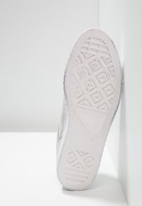 Biała sneakerowa podeszwa z teksturowaną gumową podeszwą, która ma geometryczne wzory. Miękkie szare tekstylne boki z dyskretnym detalem marki.