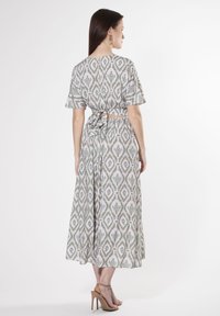Midi-Kleid aus gemustertem Stoff; mit kurzen Ärmeln, einer Rückbandage und einem cremefarbenen Grundton mit grünen geometrischen Druckmustern. Abgerundet mit Riemchenhighheels.
