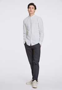 Witte linnen overhemd met een mandarin-kraag en een borstzak, gecombineerd met donkere broek en lichte sneakers. Soepele textuur.