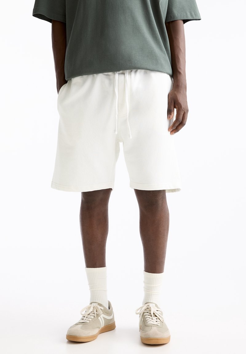 Shorts en coton blancs avec une taille élastique à cordon, associés à un haut ample vert à manches courtes et des baskets beiges. Tenue simple et décontractée.
