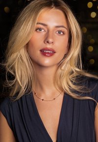 Goldene Halskette mit geometrischen Akzenten in Bernstein- und klaren Farbtönen. Getragen mit einem dunkelblauen Oberteil, vor einem sanft beleuchteten Hintergrund.