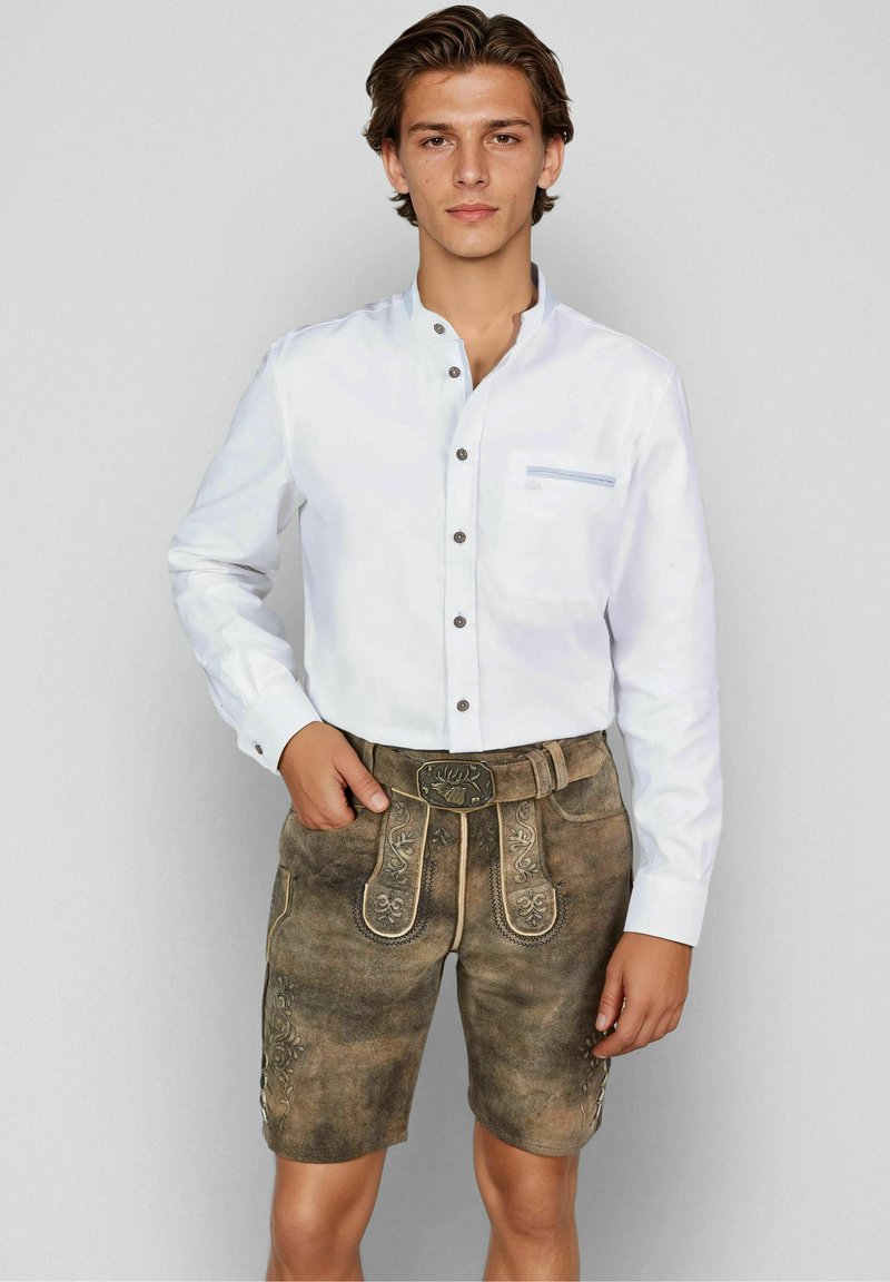 Jeune homme portant une chemise blanche à boutons avec col mandarin et un short en cuir marron brodé, agrémenté d'une boucle de ceinture décorative.