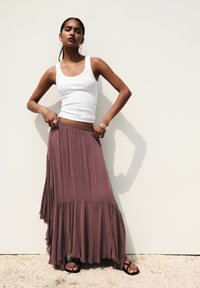 Long, flowing, rust-colored skirt with a ruffled hem, paired with a fitted white tank top and black sandals. adorned with silver bangles.