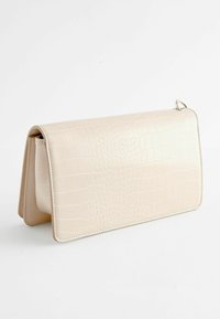 Pochette en cuir gaufré crocodile beige avec une texture lisse, de forme rectangulaire et une fermeture à rabat. Dispose de quincaillerie couleur argent.