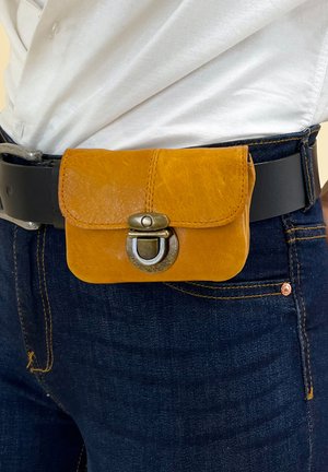 Yellow leather pouch on a black belt, featuring a metal clasp. Pouch has a rounded shape and a smooth texture. Worn above dark blue jeans.