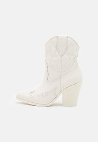 Białe skórzane kowbojskie buty z ostro zakończonym noskiem, ozdobnym haftem i grubym, prostokątnym obcasem na jednolitym białym tle.