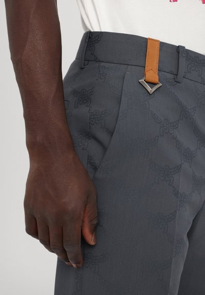 Pantalons gris à motifs avec un tissu texturé. Présente une sangle en cuir et un accent en métal argenté au niveau de la taille.