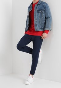 Denimjack met blauwe wassing, rood shirt met lange mouwen, marineblauwe joggers en witte sneakers. Eenvoudig ontwerp met een relaxte pasvorm en minimale hardware.