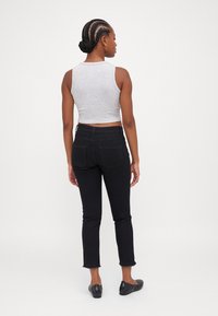 Siva bezrukavni crop top, crne traperice visokog struka s isčupanim rubom i crne balerinke. Glatka tekstura i prilagođeni dizajn. Pogled s leđa.