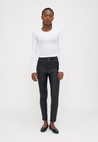 Witte langekorte mouwtop en zwarte high-waisted broek met ritsmanchetten. Glad stof met een aansluitend ontwerp en twee voorknopen.
