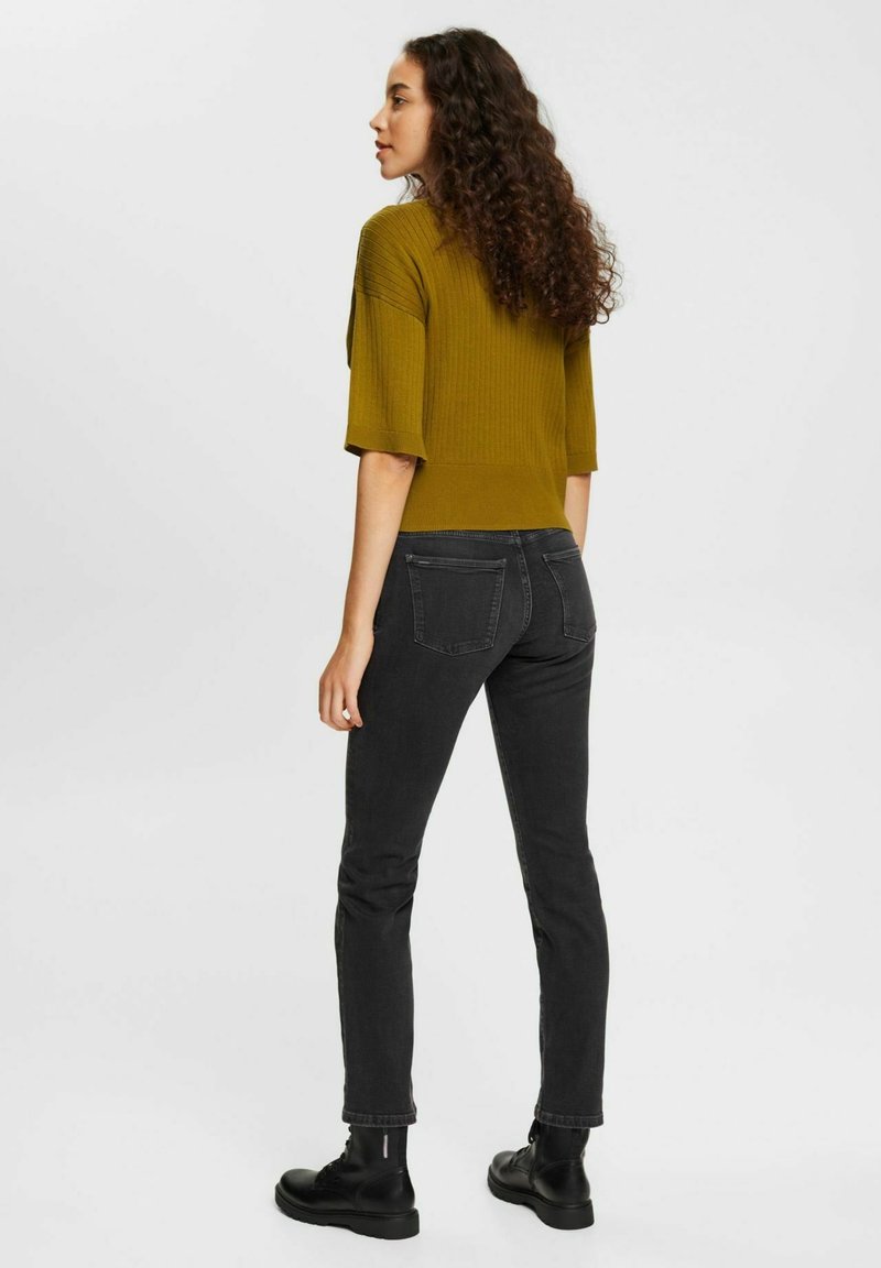 Haut en tricot côtelé couleur moutarde avec un design court, associé à un jean slim noir et des bottes à lacets noires. Look simple et fonctionnel.