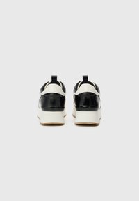 Black and white sneakers with a glossy upper, featuring a textured heel accent and a beige sole. Logo embossed at the back.