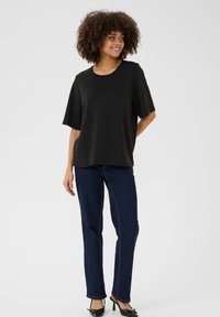 Svart oversized t-shirt med korta ärmar, rund halsringning, mjuk textur, kombinerad med mörkblå jeans och svarta spetsiga klackar.