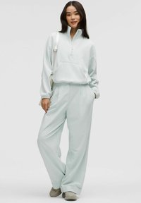 Tuta verde menta chiaro con pullover a mezza zip e pantaloni a gamba larga; tessuto morbido, vestibilità rilassata e dettaglio con tasca a marsupio.