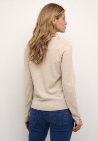 Beige sweater with long sleeves, round neckline, ribbed hem and cuffs. Worn with blue denim jeans featuring back pockets and textured stitching.