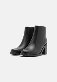 Botas negras hasta el tobillo hechas de cuero suave con punta redondeada, cremallera lateral y un tacón de bloque texturizado. Diseño sencillo sin patrones visibles.