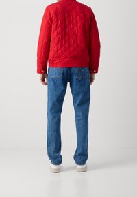 Giacca rossa trapuntata con colletto rotondo, abbinata a jeans in denim blu. L'outfit è completato da sneaker bianche.