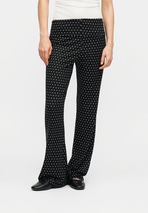 Kobieta ubrana w czarne spodnie o szerokich nogawkach w białe kropki, w połączeniu z czarnymi balerinami i białym topem.