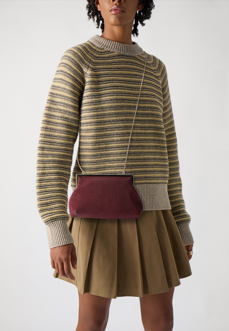 Maglione a righe giallo e grigio, abbinato a una gonna khaki piegata. Una piccola borsa a tracolla in burgundy con texture pende da una catenina.