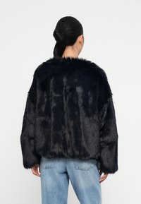 Giacca in pelliccia sintetica nera con design corto, maniche ampie e una morbida texture, abbinata a jeans chiari a vita alta.