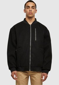 Chaqueta bomber negra con cierre delantero, puños acanalados y un bolsillo en el pecho. Fabricada con una tela suave, tiene un corte holgado y un hardware mínimo.