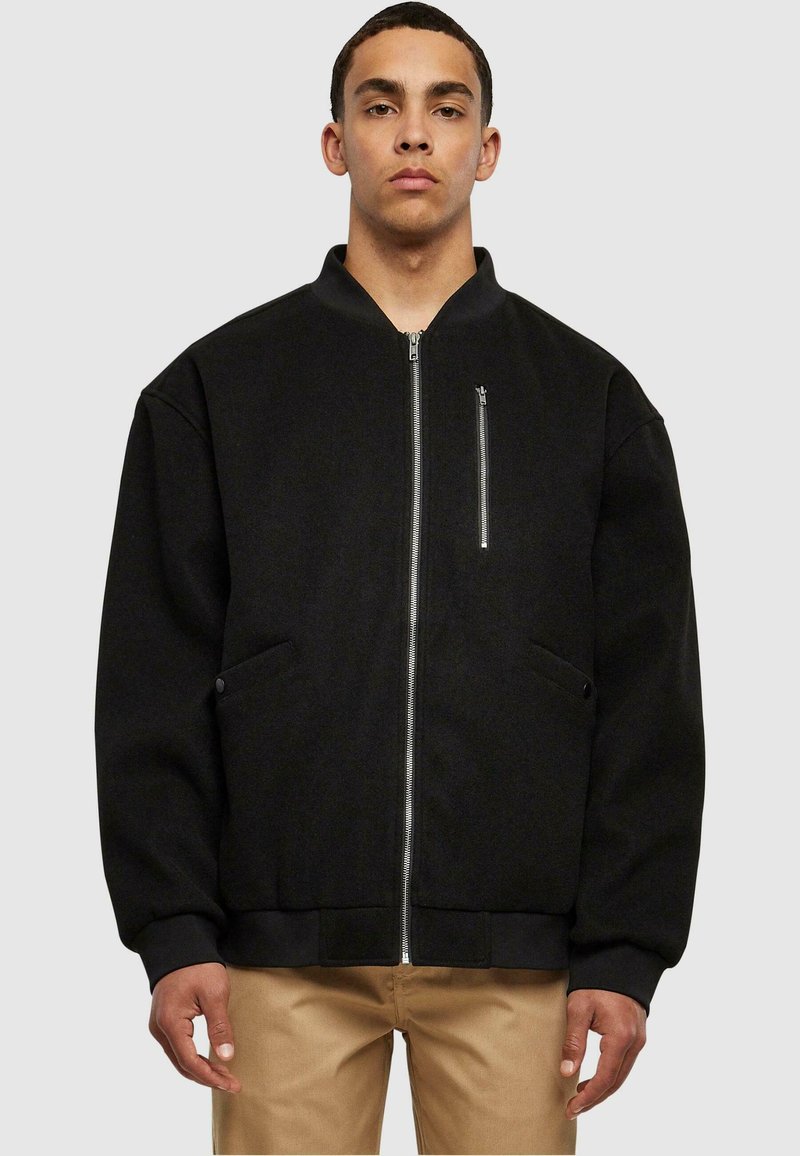 Chaqueta bomber negra con cierre delantero, puños acanalados y un bolsillo en el pecho. Fabricada con una tela suave, tiene un corte holgado y un hardware mínimo.